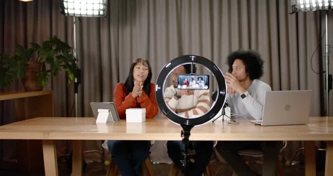 African American co-hosts starting ring light smartphone recording, showing product box at set demo