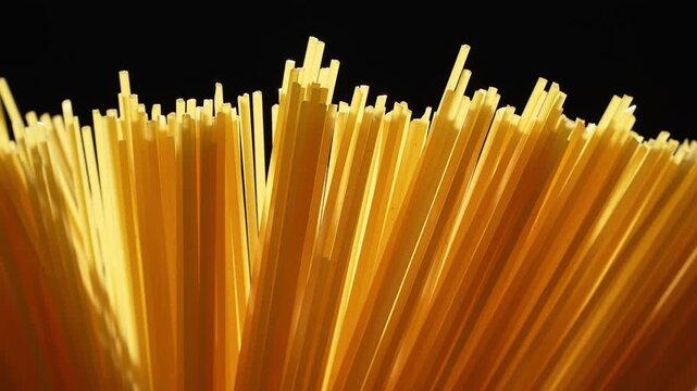 Horizontal view of dry raw spaghetti noodle tips on black background.
