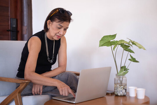Mature woman using a laptop at home, focused on browsing and digital tasks, representing technology, remote work, online learning, communication, independence, productivity, and modern lifestyle.