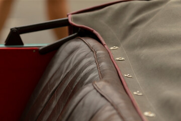 Obraz premium Close-up view of a brown quilted leather car seat partially covered by an olive canvas tonneau cover secured with brass snap fasteners. Visible folded edge