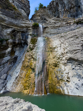 serene waterfall cascading down rocky cliff face in low angle view of natural canyon setting with green and gray tones and dramatic lighting for outdoor adventure photography.