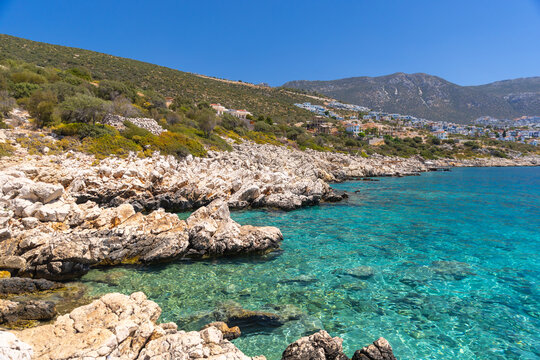 Wild beach landscape, Kalkan, Turkey.  Turquoise waters lap a rugged rocky coast while a hillside town rises along the shore. A vivid Mediterranean scene perfect for travel, nature, and seaside themes