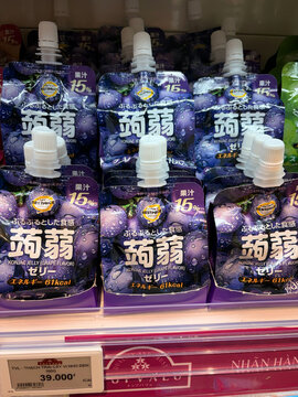 A display of grape jelly packets arranged neatly on a supermarket shelf. The packaging features vibrant purple colors with Japanese text. Convenient squeeze bottles are visible.