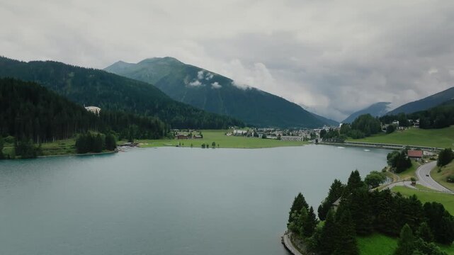 Aerial drone view of alpine lake town in mountain valley pine forests cloudy Switzerland