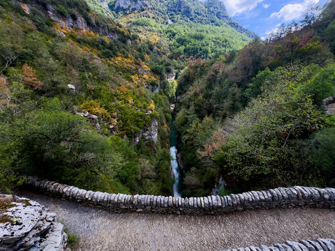 a stone bridge spans across a lush, green forested canyon with a river running through it, offering a peaceful and serene view from above the canyon floor, captured.