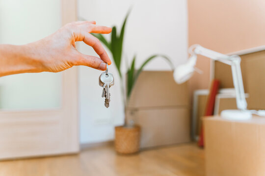 Hand holding keys with moving boxes indoors in new apartment. Relocation and residential property purchase commercial concept.
