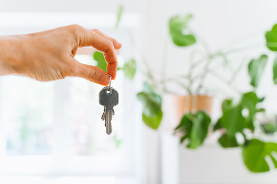 A hand holds new house keys against the blurred background of a bright modern apartment kitchen. Successful residential property purchase and exciting relocation commercial lifestyle concept.