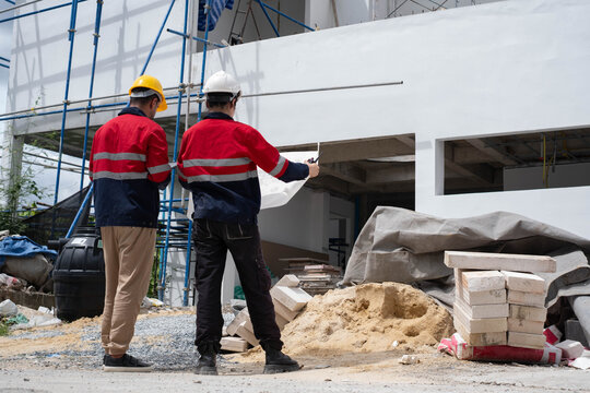 Construction engineers reviewing architectural plans at a residential building site, inspecting exterior progress, structural quality, and safety compliance for efficient project management.