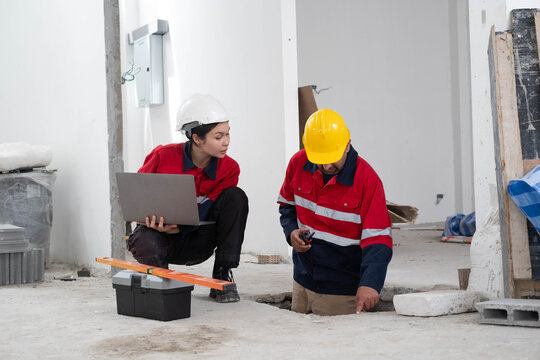 Construction engineer reviewing project data on a laptop while inspecting underground utility work with a technician during building renovation. Site safety, quality control, engineering management.