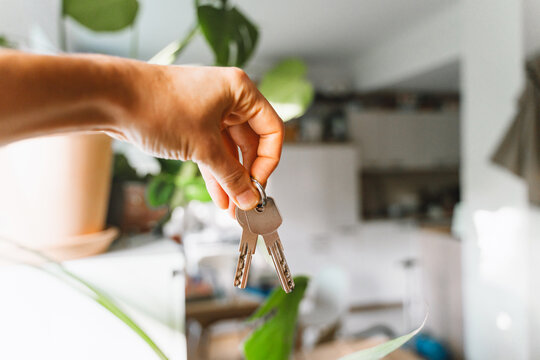 A hand holds new house keys against the blurred background of a bright modern apartment kitchen. Successful residential property purchase and exciting relocation commercial lifestyle concept.
