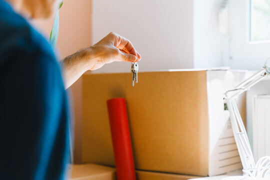 Hand holding keys with moving boxes indoors in new apartment. Relocation and residential property purchase commercial concept.