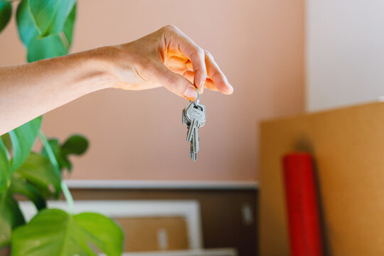 Hand holding keys with moving boxes indoors in new apartment. Relocation and residential property purchase commercial concept.