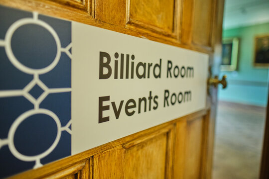 A billiard room and events room directional sign mounted on a traditional wooden panelled door in a victorian workhouse