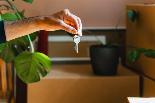 Hand holding keys with moving boxes indoors in new apartment. Relocation and residential property purchase commercial concept.