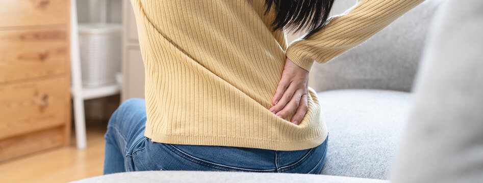 Close-up woman massaging her lower back has back pain because of sitting posture during work in office.