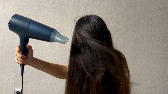 Woman drying her long hair with a hair dryer at home during a daily hair care and beauty routine