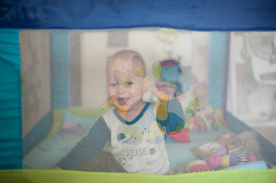 Joyful toddler with a radiant smile playing happily inside a colorful mesh safety playpen during the morning time at home while wearing comfy pajamas
