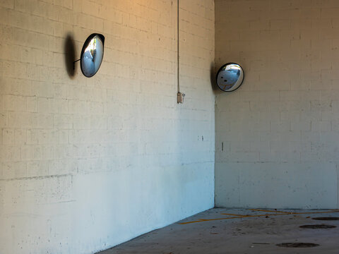 Two adjoining walls in a tight urban parking garage with convex mirrors that enable drivers to see around blind corners of a combined entry and exit. Motifs of visibility, decisions, and safety.