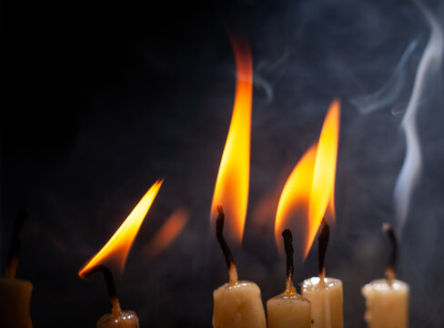 Candles burn with bright flames giving off smoke in a dark setting during a quiet moment