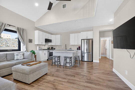 Bright open-plan kitchen with white cabinets, stainless refrigerator, marble island and wood floors