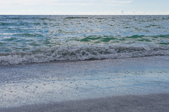 Wide view of a quiet sandy beach and shoreline in Treasure Island, FLwith gentle ocean waves, sparse shells, and distant seaside buildings under an overcast sky conveying calm, solitude, and coastal a