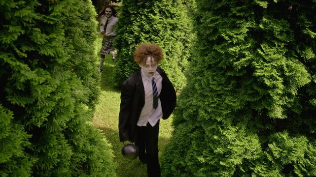 Diverse group of teenagers in Halloween zombie costumes running through green hedge maze outdoors. Footage suitable for autumn seasonal advertising and holiday youth campaigns