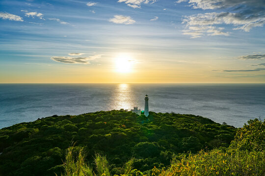 Golden light cascades over the historic Cape Bojeador Lighthouse as the sun dips into the horizon above the tranquil waters of the Luzon Sea at dusk