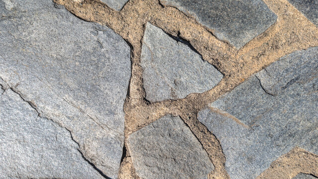 Natural stone paving texture with grey irregular slabs and sandy mortar filling the gaps, background, texture