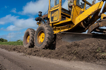 Fototapeta premium Yellow motor grader pushing and leveling soil on a rural dirt road