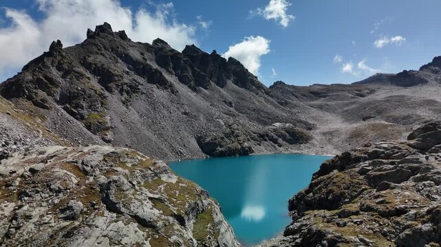 Aerial drone view of a turquoise alpine lake below jagged rocky peaks at Pizol, Switzerland