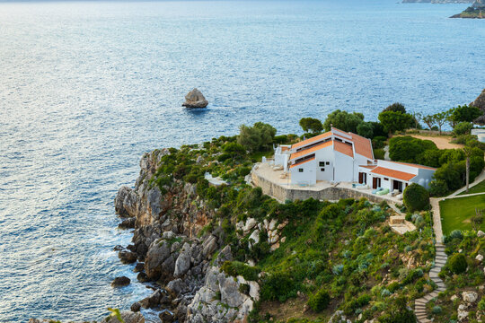Stunning coastal landscape featuring a modern Mediterranean house surrounded by lush greenery and blue water