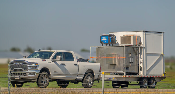 Calgary, AB, Canada - Sept 15, 2026: White Ram pickup truck towing a flatbed trailer with heavy industrial equipment along a highway.