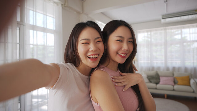 Two young Asian women smiling and posing together for a selfie with smartphone at home