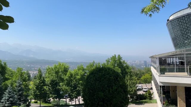 Scenic View of Almaty Kazakhstan with Green Park Trees, Cityscape and Snow Capped Tien Shan Mountains in the Background on a Clear Summer Day