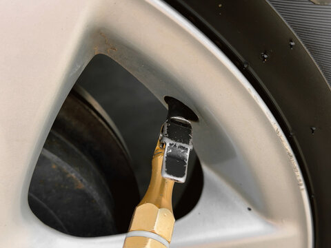 Car tire inflator nozzle attached to a wheel valve for checking air pressure.