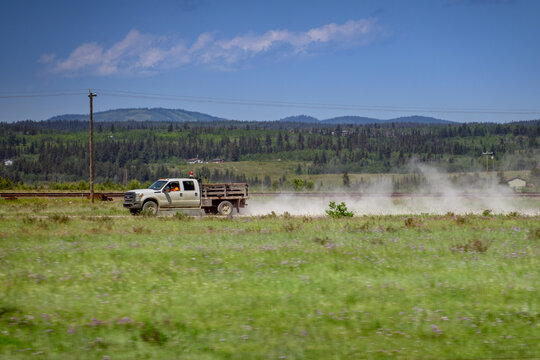 Calgary, AB, Canada - Sept 15, 2026: White flatbed pickup truck driving along a rural gravel road kicking up a cloud of dust.