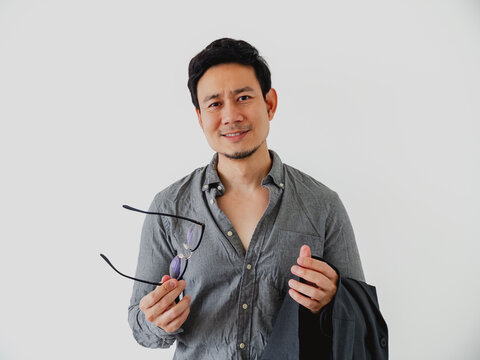 Confident Asian Man Holding Eyeglasses and Jacket, Smiling Casually Against a White Background