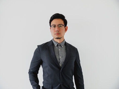 Serious Asian businessman in a dark suit and glasses standing confidently against a white background