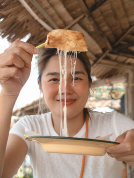 Young Asian Woman Happily Showing a Delicious Cheese Pull from a Warm Pastry Snack