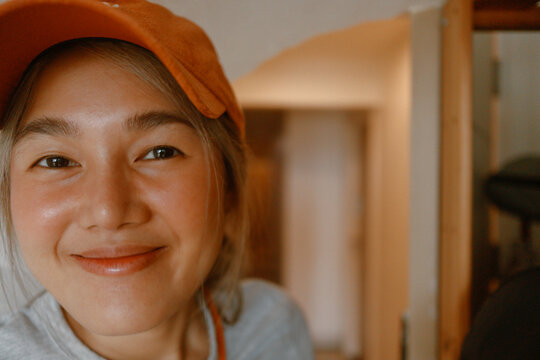 Close-up Portrait of a Smiling Young Asian Woman Wearing an Orange Cap Indoors