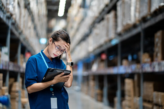 Female Warehouse Manager Pressing Her Hand Against Her Head with a Stressed Expression While Holding a Digital Tablet. Work-Related Stress, Managerial Fatigue, Warehouse Operational Pressure