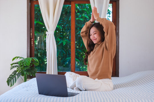 Portrait of a woman meditating or practicing yoga on bed in front of laptop computer