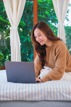 Vertical portrait of a woman using and working on laptop computer while sitting on bed at home
