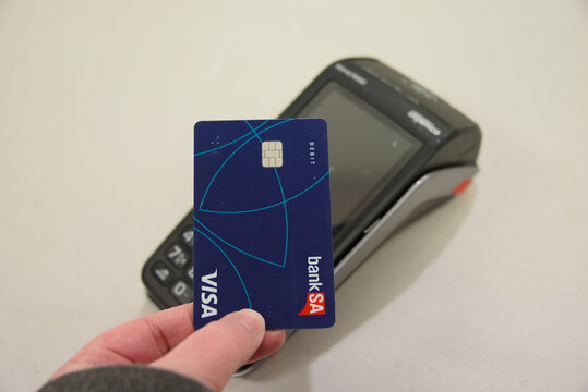 Semaphore, South Australia - July 22 2026: hand holding a debit card near a point of sale terminal for a financial transaction
