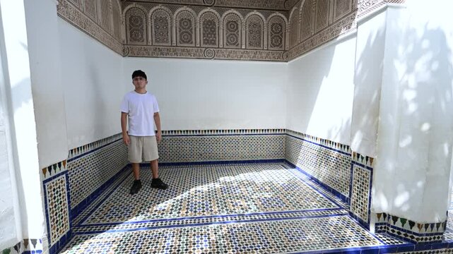 Marrakech, morocco. August 10, 2026. Young man visiting the historic bahia palace in marrakech, morocco. Sunlight shines on the beautiful zellij mosaic tiles of the room