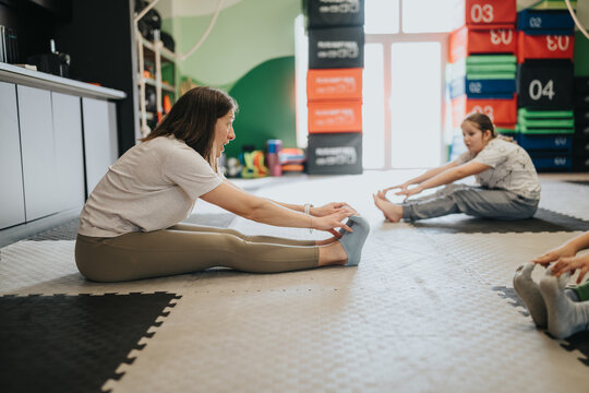A woman and children perform seated hamstring stretches on floor mats in a fitness studio. A teacher leads kids through gentle stretches in a colorful gym setting.