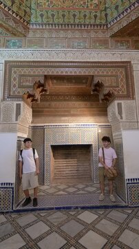 Marrakech, morocco. August 10, 2026. Two young male travelers standing inside a room of the historic bahia palace, admiring the intricate moroccan zellij mosaic tiles and patterns