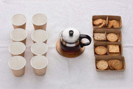 Overhead view of coffee break with disposable paper cups, teapot, and assorted cookies.