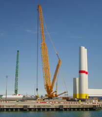 Fototapeta premium Giant Crawler Crane Assembling Wind Turbine Tower Sections at Port Harbor, Sustainable Offshore Renewable Energy Construction and Logistics