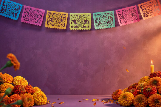 Day of the Dead festive background with hanging colorful papel picado banners, mounds of orange marigolds, and glowing candle